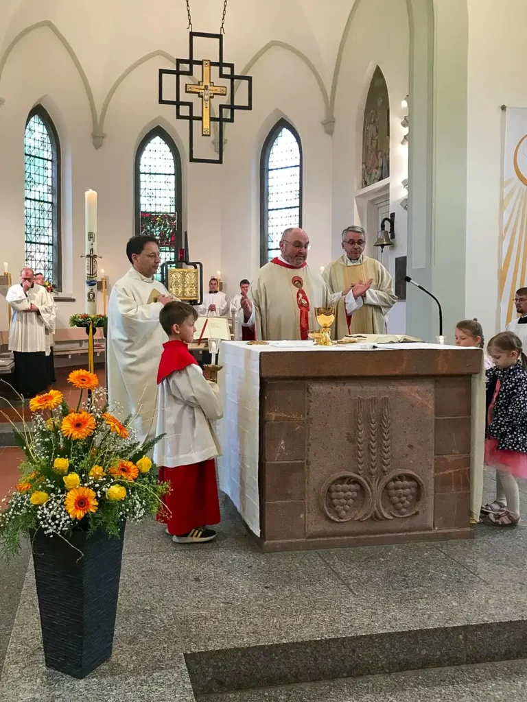 Pater Ensch während der Messe am Altar, links ein Messdiener, rechts zwei Kinder, im Hintergrund weitere Geistliche