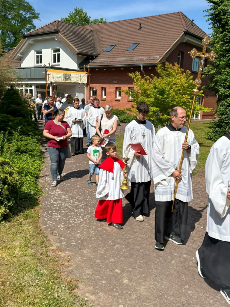 Prozession der Gemeinde, im Vordergrund Messdiener mit Kreuz und Kerze, hinten der Pfarrer unter einem Baldachin