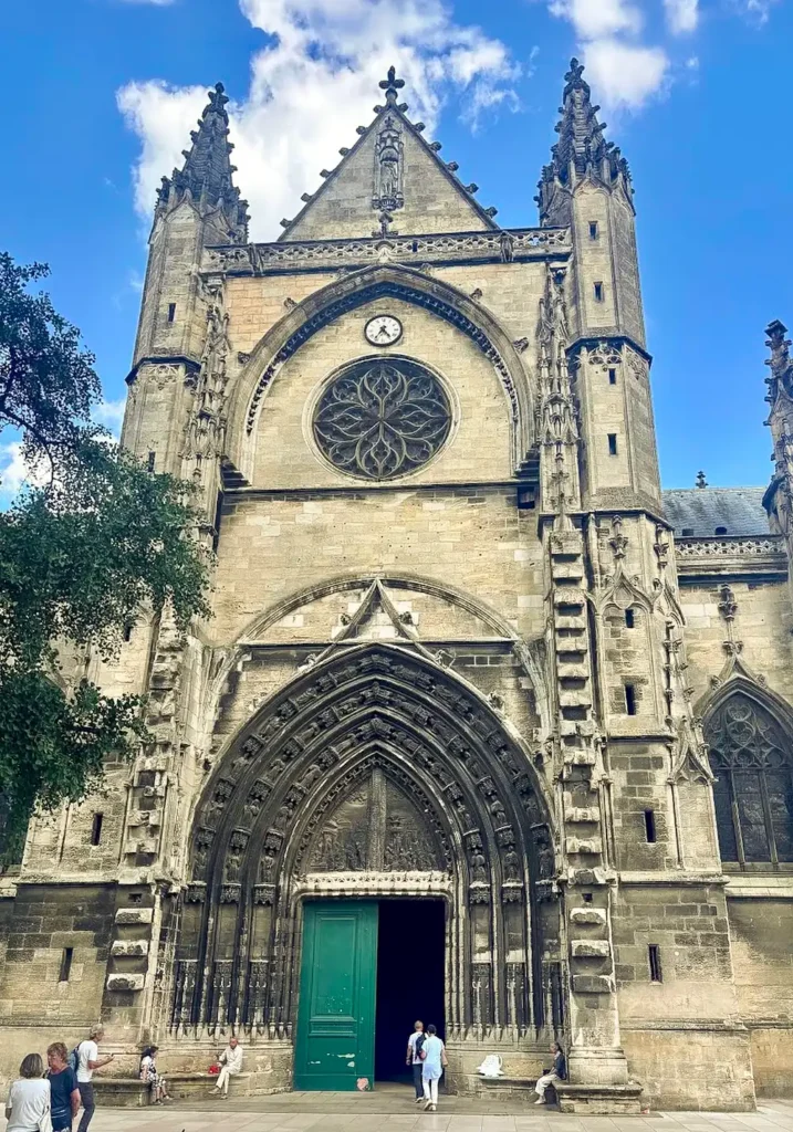 Frontansicht der Basilika Saint-Seurin unter einem sonnigen Himmel, die Tür ist geöffnet und zwei Menschen gehen hinein.