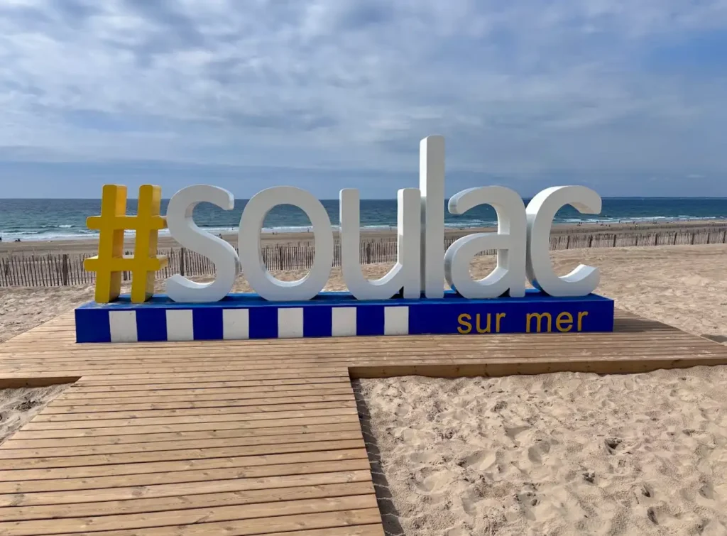 Strandansicht mit einem großen Schild im Vordergrund, auf diesem steht "#soulac sur mer"